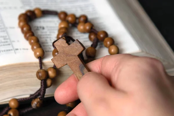 Woman holding and praying on rosary, on Bible background.