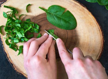 Bir kadın kesme tahtasına taze ıspanak kesiyor..