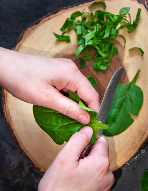 Bir kadın kesme tahtasına taze ıspanak kesiyor..