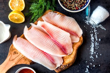 Siyah arka planda baharatlı ve limonlu çiğ tilapia fileto..