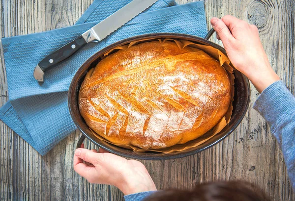 Hands holding a pan of freshly baked bread, top view