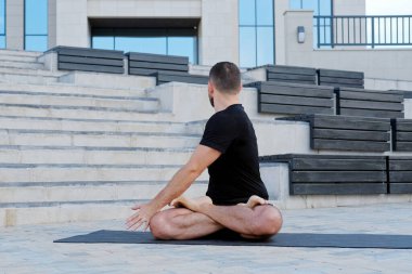 Siyah spor kıyafetleri giyen erkek sporcu yoga egzersizleri, esneme hareketleri, fitness, nilüfer pozisyonu, savaşçı duruşu yapıyor.