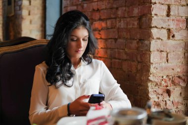 Kafedeki iş kadını akıllı telefon kullanıyor ve gülümsüyor..