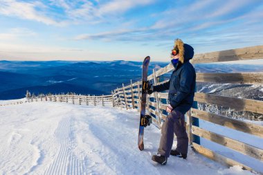 Sheregesh dağlarında başarılı bir snowboard sporcusu. Snowboardcu dağın tepesinde dinleniyor. Mavi gökyüzünün arka planında beyaz bir snowboardcu. Beyaz kaykaycı, şık biri. kayak merkezi