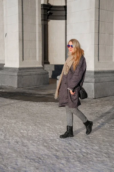 一个穿着灰色外套和太阳镜的漂亮女人走在城里的大街上 图库图片