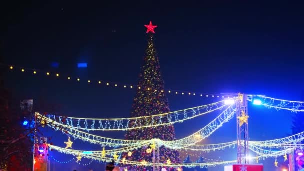 Novosibirsk, Rusia, 31.12.2020: La gente monta en una pista de patinaje alrededor del árbol de Navidad con estrella roja. La decoración de Año Nuevo de la guirnalda de la ciudad — Vídeos de Stock