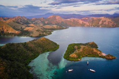 Komodo Takımadası 'ndaki Strawberry Rock pembe-turuncu uçurumları, turkuaz denizi ve yemyeşil mangrov bitkilerini gösteriyor. Endonezya 'nın çarpıcı doğal bir simgesi ve Komodo Ulusal Parkı' nın eşsiz bir manzarası..