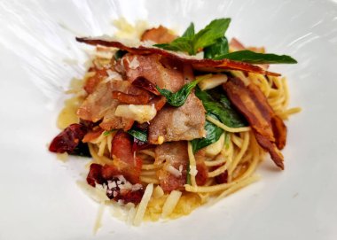 Kızarmış spagettiyi, kurutulmuş biberli ve beyaz tabakta kızarmış pastırmayla yakından incele..