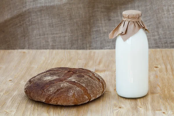 Roggebrood met fles melk op houten tafel — Stockfoto