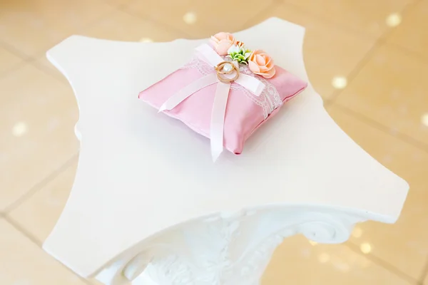Anéis de casamento dourados no travesseiro branco decorado com flores — Fotografia de Stock