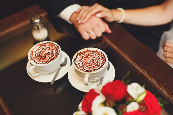 Mãos de noiva e noivo na mesa, xícaras de café latte — Fotografia de Stock