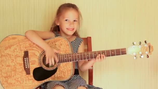Милая маленькая девочка играет на акустической гитаре и качает головой — стоковое видео