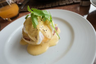 Yumurta Benedict haşlanmış domuz pastırması hollandaise sos yumurta beyaz plaka üzerinde.
