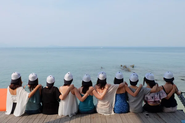 Gruppo di dieci amiche sedute abbracciano insieme cielo blu del mare. Indossano lo stesso design berretti in bianco e nero . — Foto Stock