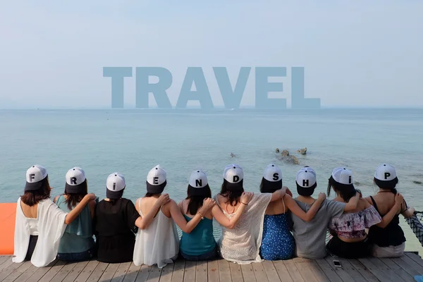 Grupo de diez mujeres amigas se sientan juntos abrazo mirada VIAJE azul cielo marino. Llevan las mismas gorras de diseño con alfabetos de amistad . — Foto de Stock