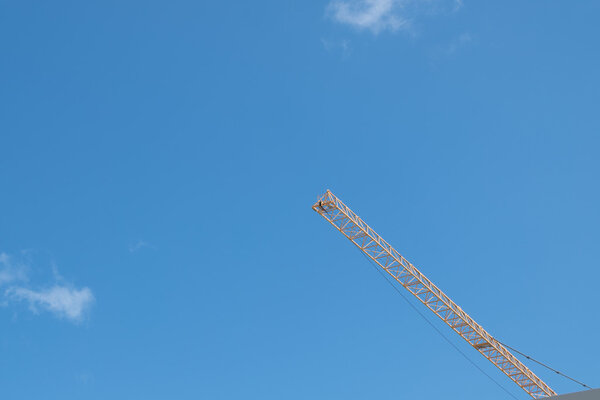 Nice color combination of yellow high long crane arrow at construction site and clear light blue sky day.