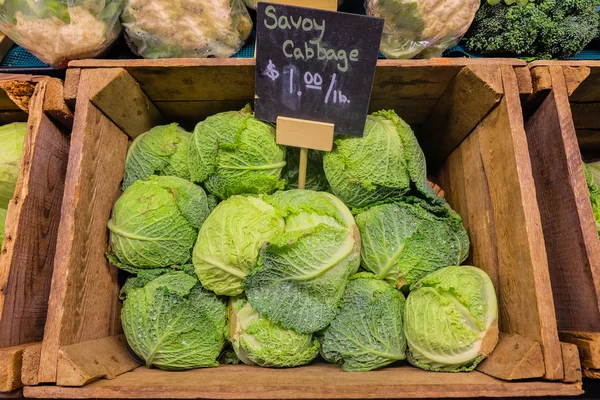 Čerstvé zelí zelenina v dřevěné stáje a v greengrocery s popiskem tabuli cenu. — Stock fotografie