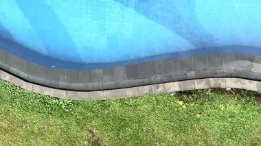 Yeşil çimlerin yanında kıvrımlı kenarları olan mavi bir yüzme havuzunun havadan görüntüsü. Sahne, sakin su, temiz fayanslar ve sakin bir açık hava havasını gösteriyor. Seyahat, tatil, spa, tatil beldesi veya yaz rahatlama kavramları için idealdir.