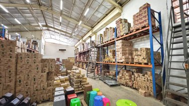 Jakarta, Endonezya, 19 Ocak 2026: Çeşitli yiyecek ve içecek kutularıyla dolu büyük bir depo. Metal raflar ve zemin düzenlemeleri aktif envanter sistemlerine sahip iyi organize edilmiş bir dağıtım merkezi gösteriyor.