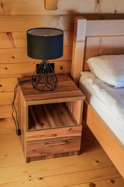 Beyaz ahşap bir yatağın yanında siyah lambalı ahşap bir komodinin yakın çekim görüntüsü. Detaylara odaklan, rahat iç mekan, doğal gün ışığı, köylü tarzı..