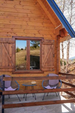Ahşap bir eko evde teras, sandalyeler ve bir masa. Doğal ışık, konforlu ve sürdürülebilir tasarım, kırsal atmosfer.