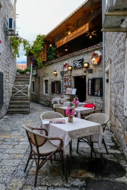 Karadağ 'ın tarihi Budva kentinde deniz temalı dekorun yer aldığı bir kafenin editör fotoğrafı 4 Aralık 2025' te çekildi. Dar taş sokaklardaki masaları, sandalyeleri, deniz dekorasyonlarını ve atmosferik ışıklandırmayı gösteriyor. Uygun.