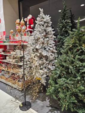 Bir alışveriş merkezinin içinde Noel Baba figürünün yanında çeşitli şekillerde süslenmiş Noel ağaçları. Bayram süslerini, mevsimlik gösterileri ve Noel alışverişinin neşeli atmosferini gösteren şenlikli sahneler..