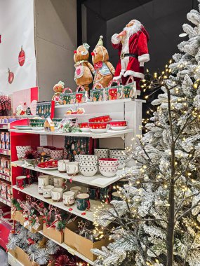 Noel Baba figürünün yanında çeşitli şekillerde süslenmiş Noel ağaçları ve çeşitli sofra takımları bir mağaza rafında sergileniyor. Bayram gösterileri, mevsimlik dekorasyonlar ve Noel alışverişi için ideal bir perakende satış sahnesi..