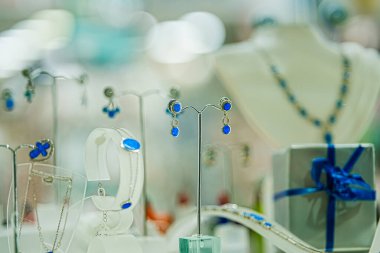 Mağaza vitrininde mavi takı küpeleri ve kolye var. Moda, hediye ve yaşam tarzı kavramları için uygun bir perakende sergisi olarak sunulan şık aksesuarlar.