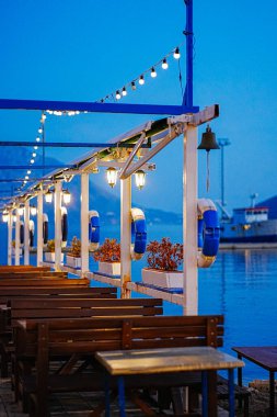 Akşamları deniz kenarında boş bir terasın dikey çekimi. Masalar boş ve cankurtaran şamandıraları kıyı atmosferi için dekore edilmiş. Seyahat, yaşam tarzı veya tatil içeriği için uygun.