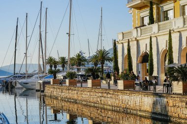 1 Ocak 2026 'da Karadağ' ın Tivat marinasının palmiye kenarı kıyısındaki kafelerde, liman ve güneşli kış atmosferinde yatlarla oturan insanların editör fotoğrafı.