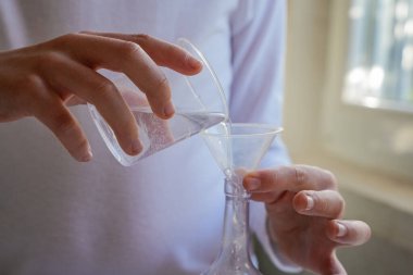 Cam bir şişeye sıvı döken aşırı yakın plan eller. Görünmez yüz.