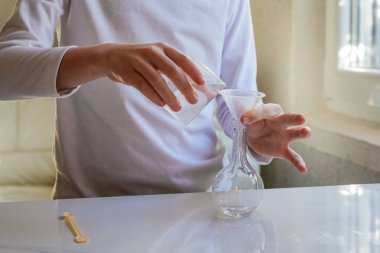 Elleri ölçü kabından cam şişeye sıvı döküyor. Görünmez yüz.