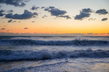 Gün batımında denizde güçlü kış fırtınası dalgaları. Dramatik gökyüzü renkleri, sert su ve soğuk hava atmosferi yoğun bir doğal deniz manzarası yaratır.