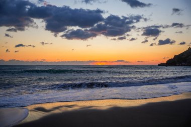Kış denizi üzerinde dalgalı turuncu gün batımı. Dramatik akşam ışığı, soğuk mevsimlik atmosfer ve karamsar kıyı manzarası..