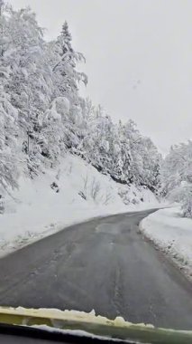 Manzaralı viraj yolu güzel bir kış manzarasının içinden geçiyor. Karla kaplı çevre ve sakin mevsimsel atmosfer huzurlu bir seyahat sahnesi yaratır..