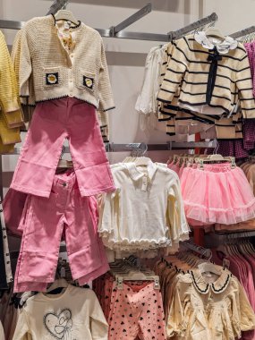 Çocuk bölümündeki askılarda pembe pantolon ve beyaz ya da çıplak süveter bulunan çocuk kıyafetleri sergileniyor. Butik tarzında perakende kurulumu.