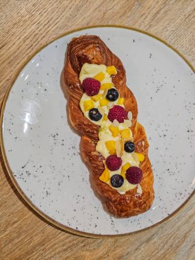 Taze ahududu ve kremalı yaban mersinli örülmüş tart tabakta servis edilir. Yemek fotoğrafçılığı, mutfak içeriği ve yaşam tarzı için ideal bir tatlı ve fırın konsepti.