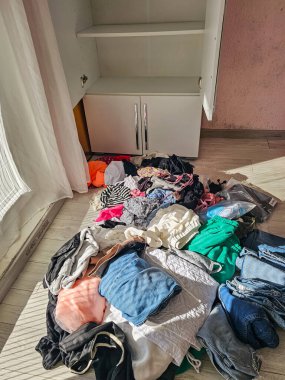 Giysiler boş bir dolabın yanına saçılmış. Dağınıklık, taşınma, temizlik, organizasyon ya da depo eksikliği kavramı. Yaşam tarzı ve ev içi temalar için elverişli.