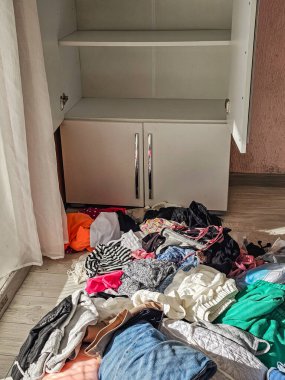 Dolapta boş raflar ve yerde giysiler var. Düzensizliği temsil eden iç mekan, temizlik günü, taşınma süreci veya ev hayatı durumu.