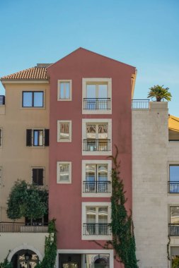 Pencereleri ve balkonunda palmiye ağacı olan bir bina manzarası. Parlak Akdeniz mimarisi ve yeşillik manzaralı bir şehir ve kıyı atmosferi yaratıyor. Seyahat, yaşam tarzı, mimari ve gayrimenkul içeriği için ideal.