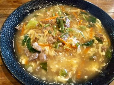 Halal Kuey Teow ya da Endonezya usulü Asya usulü erişteli sığır eti, yumurta ve sebzeli ahşap arka planda büyük bir tabak.