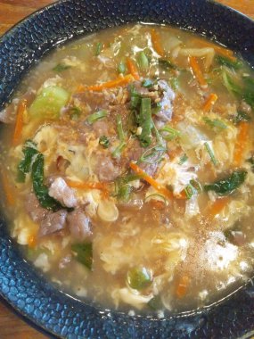 Halal Kuey Teow ya da Endonezya usulü Asya usulü erişteli sığır eti, yumurta ve sebzeli ahşap arka planda büyük bir tabak.