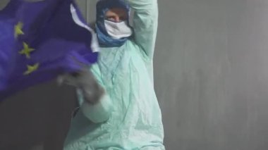 Avrupa bayrağı taşıyan kişisel koruyucu ekipman giymiş bir adam. Roman Coronavirus 2019-NCoV. Salgın durumu.