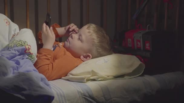 3 years old child boy using smartphone at night in bed — Stock Video