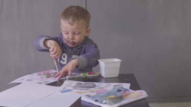 Kesik yüzlü komik bir çocuk renkli boyalarla resim çiziyor. — Stok video