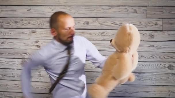 彼のオフィスでぬいぐるみクマのおもちゃを破って若い怒っているビジネスマン。フラストレーションをテーマにしたコンサート — ストック動画