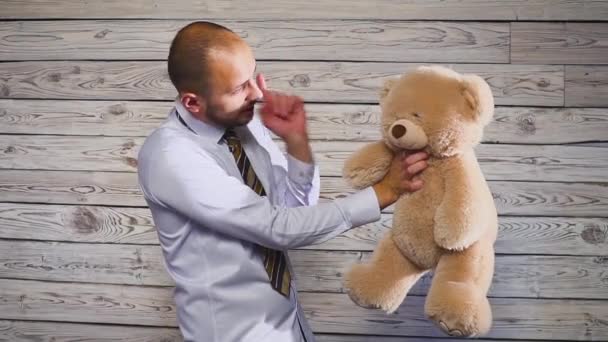 Молодой злой бизнесмен избивает плюшевую медвежью игрушку в своем офисе. Концерт на тему разочарования — стоковое видео