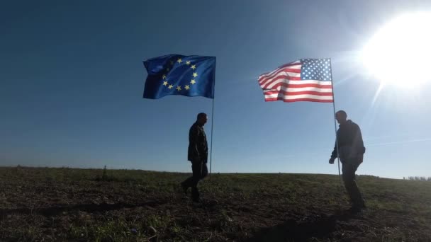 Koncepcja stosunków międzynarodowych, międzynarodowe partnerstwo USA i Unii Europejskiej. Sylwetka dwóch mężczyzn na tle flagi amerykańskiej i europejskiej. — Wideo stockowe