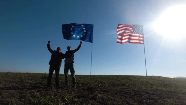 A nemzetközi kapcsolatok koncepciója, az Egyesült Államok és az Európai Unió nemzetközi partnersége. Két férfi sziluettje az amerikai és az európai zászló hátterében. — Stock videók